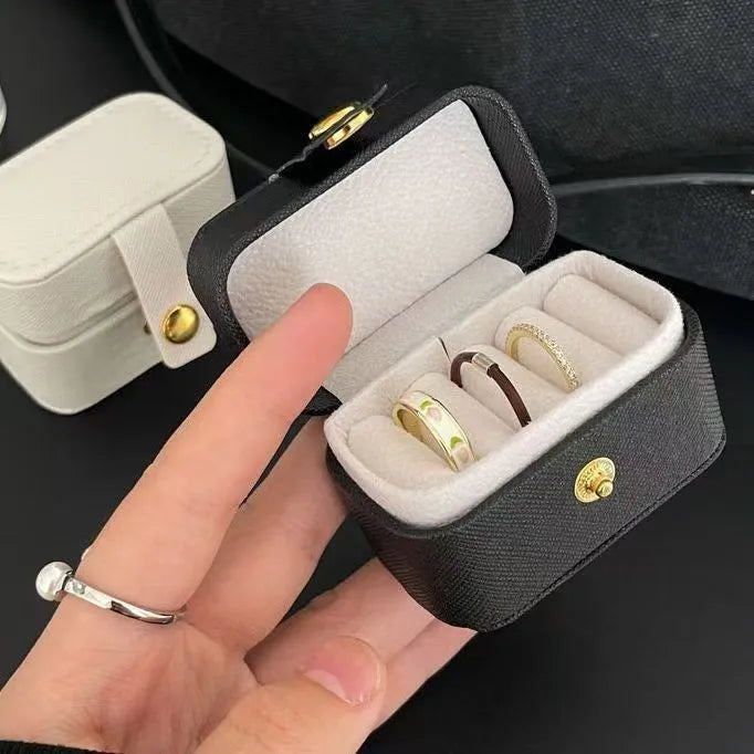 A hand holds an open black leather jewelry storage box with a white insert and gold accents.