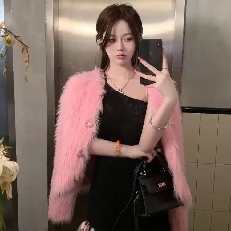 A woman wearing a pink faux fur jacket over a black top and holding a smartphone.
