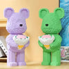 A purple and green flower bear figure made of micro building blocks stands on a wooden surface.