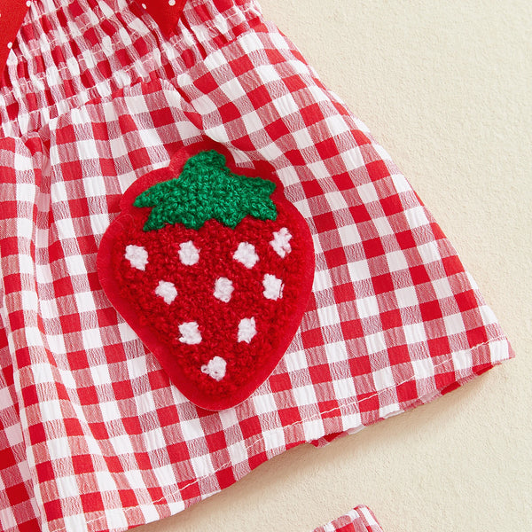 A red and white checkered fabric featuring a large, embroidered green strawberry patch.