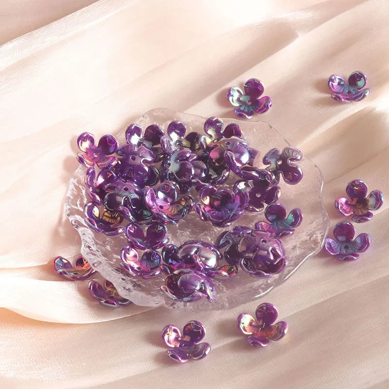 A pile of purple acrylic flower beads is displayed on a light fabric surface.