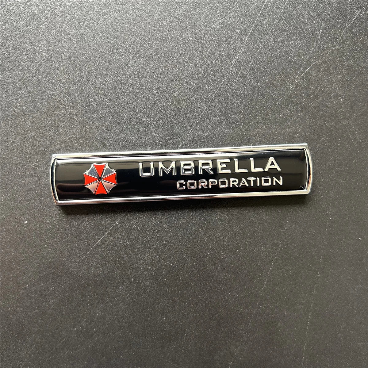 A black metal badge with the text UMBRELLA CORPORATION and a red and silver umbrella emblem.