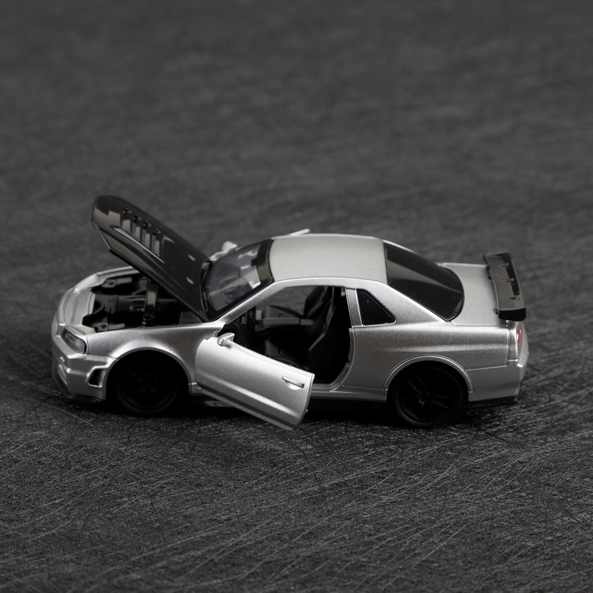 A silver die-cast sports car with the hood open, shown in a side profile against a dark background.