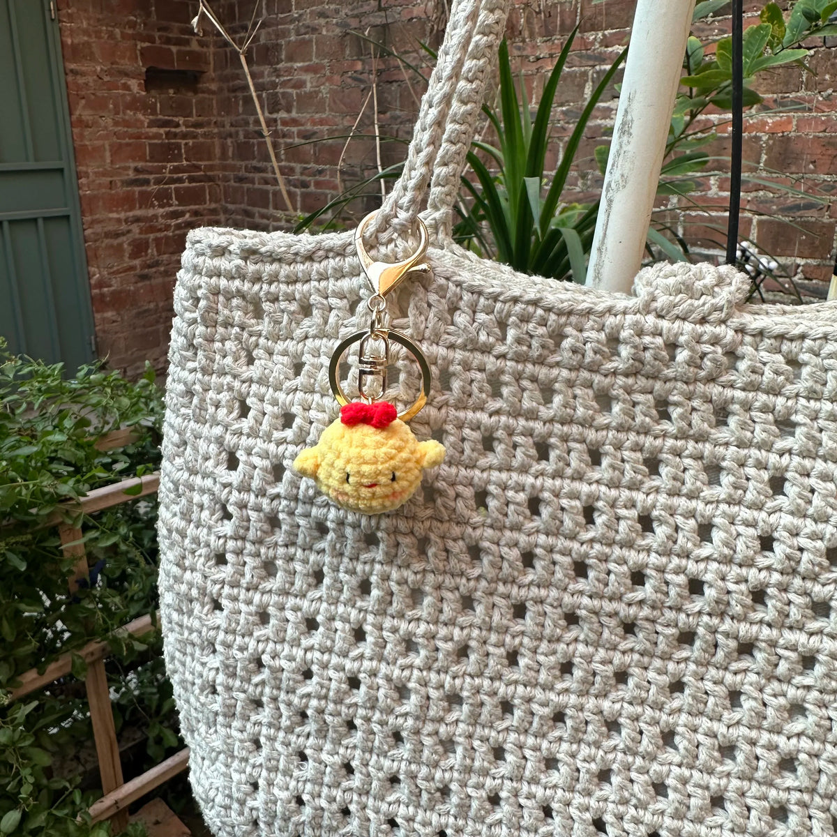 A handcrafted crochet animal keychain featuring a yellow rabbit or chick charm hanging from a gold-toned metal loop.