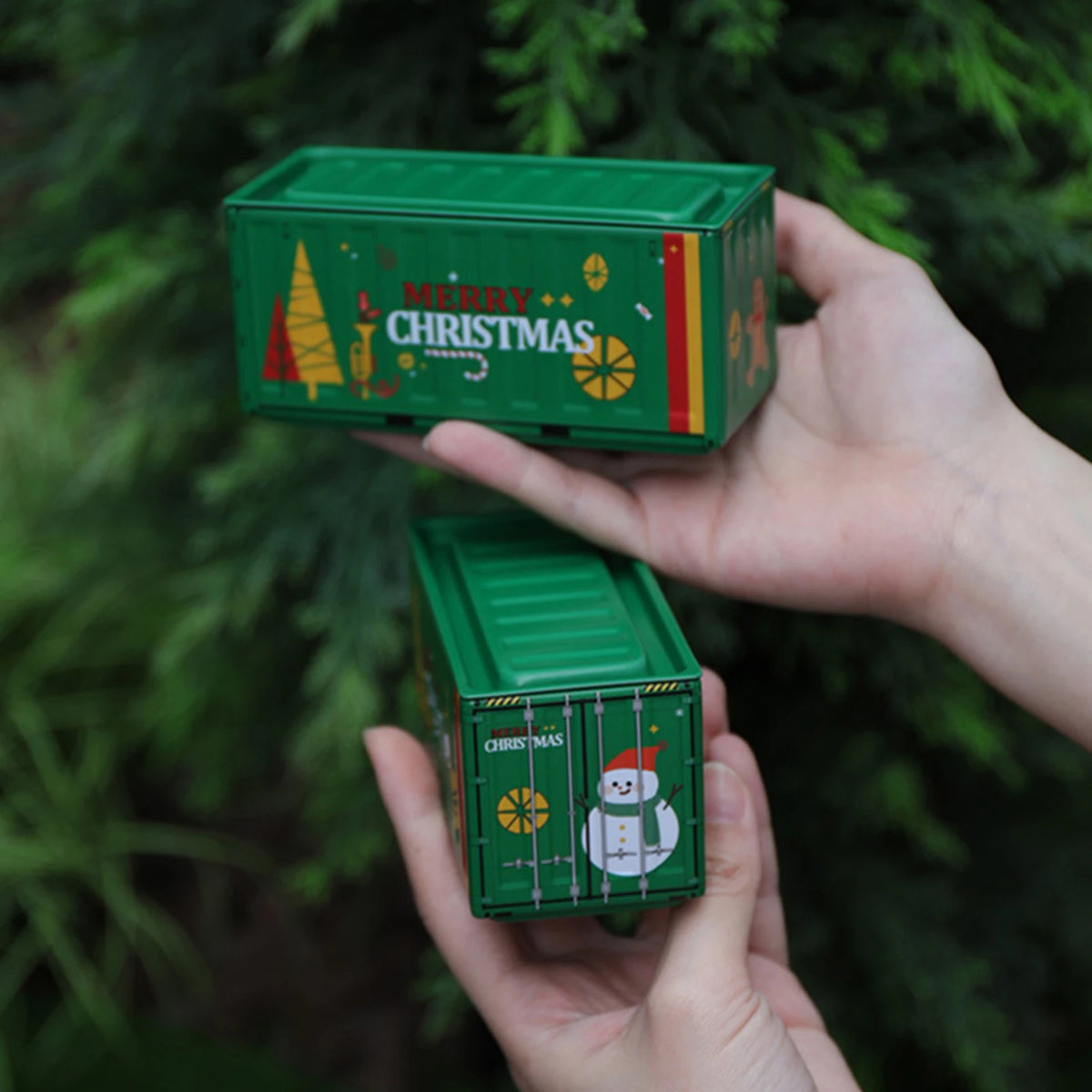 A hand holds a green miniature industrial iron storage box with an openable lid against a blurred green background.