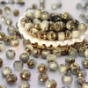 A pile of round, iridescent beads in various shades of gold and cream are scattered on a white surface.