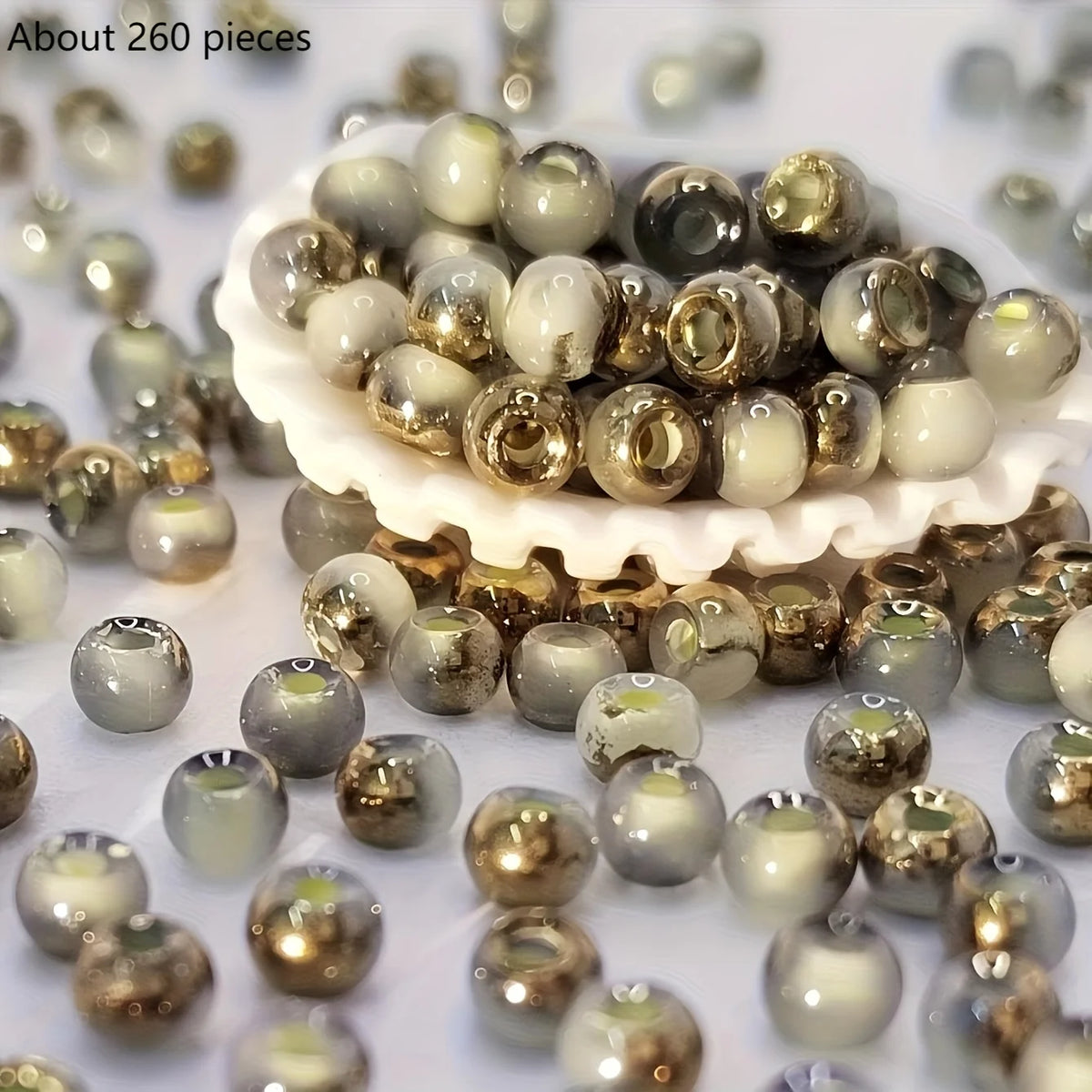 A pile of round, iridescent beads in various shades of gold and cream are scattered on a white surface.