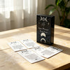 A black box of Spirit Messages Oracle Cards with silver symbols rests on a wooden table.