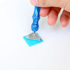 A hand holds a blue resin diamond painting pen set with a threaded dotting tip and a silver holder.