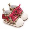A pair of leopard print baby sneakers with pink laces and a red bow.