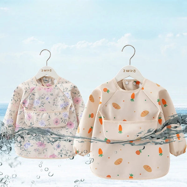 A light beige toddler feeding bib with long sleeves and a floral pattern is displayed on a hanger against a blue sky backgrou