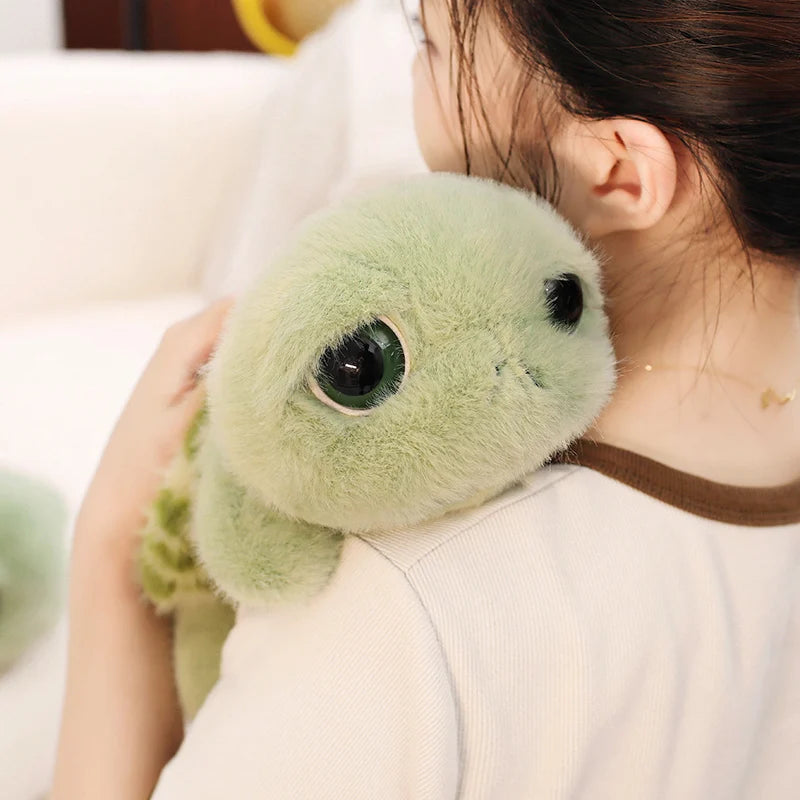 A person is holding a soft, light green plush sea turtle stuffed animal with large eyes.