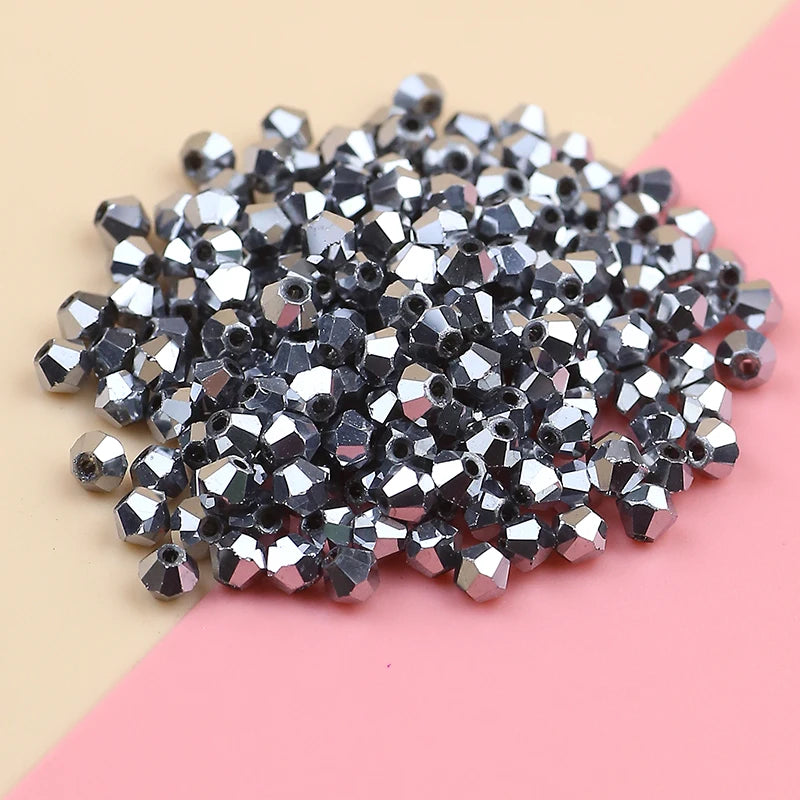 A pile of small, silver-toned electroplated crystal glass beads for jewelry making on a pink surface.