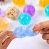 A hand holds a translucent blue squeeze ball next to several colorful, translucent stress relief balls.