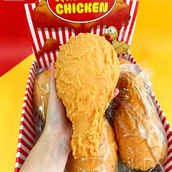 A hand is holding a realistic food squeeze toy of a chicken in a clear plastic bag, displayed in a red and white box.