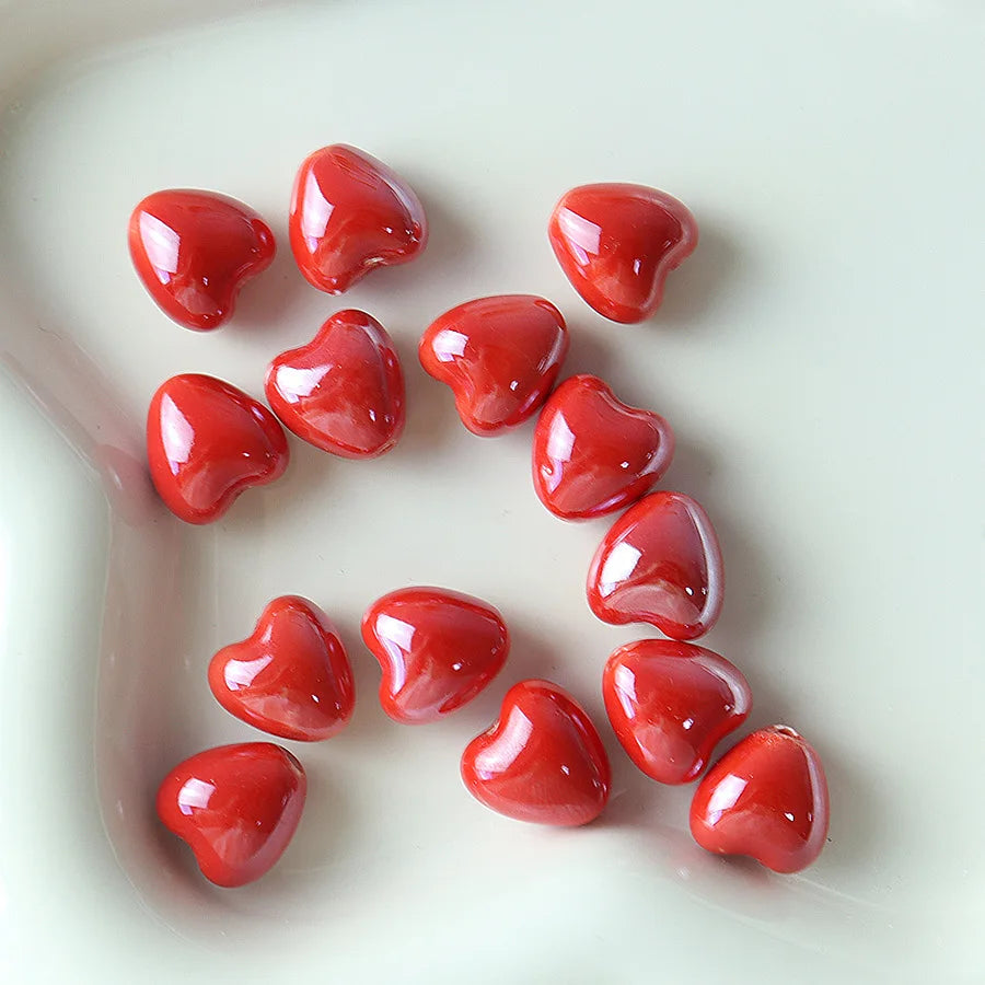 A collection of ten glossy red heart-shaped ceramic beads arranged on a white dish.