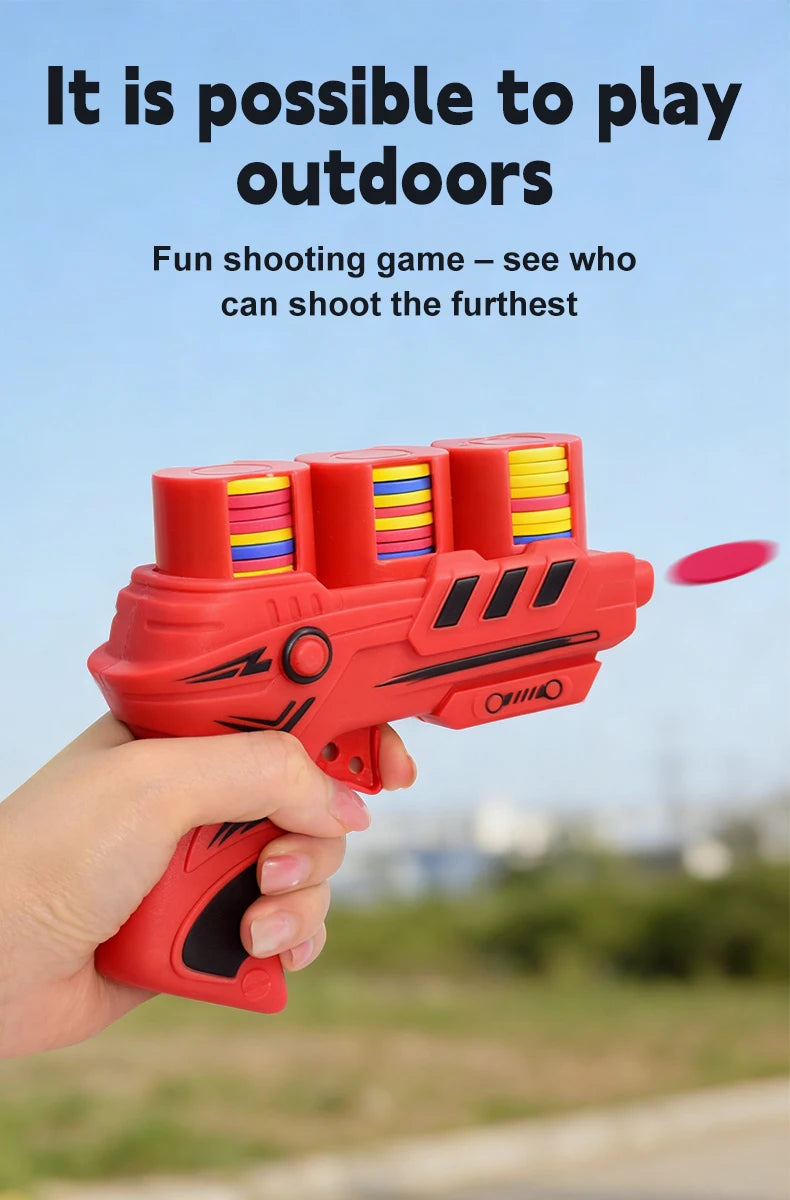 A hand holds a red soft foam flying disc launcher toy, aiming it outdoors.