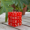 A stack of 36 transparent red and white dice set on a wooden surface next to a green plant.