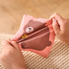 A hand is holding a soft fabric tissue box sensory toy shaped like a brown bear with a yellow flower on a beige knitted surfa