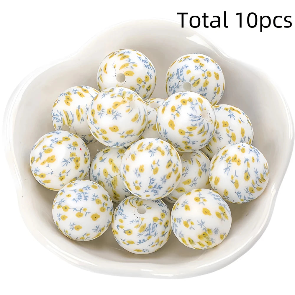 A bowl filled with ten white silicone beads decorated with yellow and blue floral patterns for DIY jewelry making