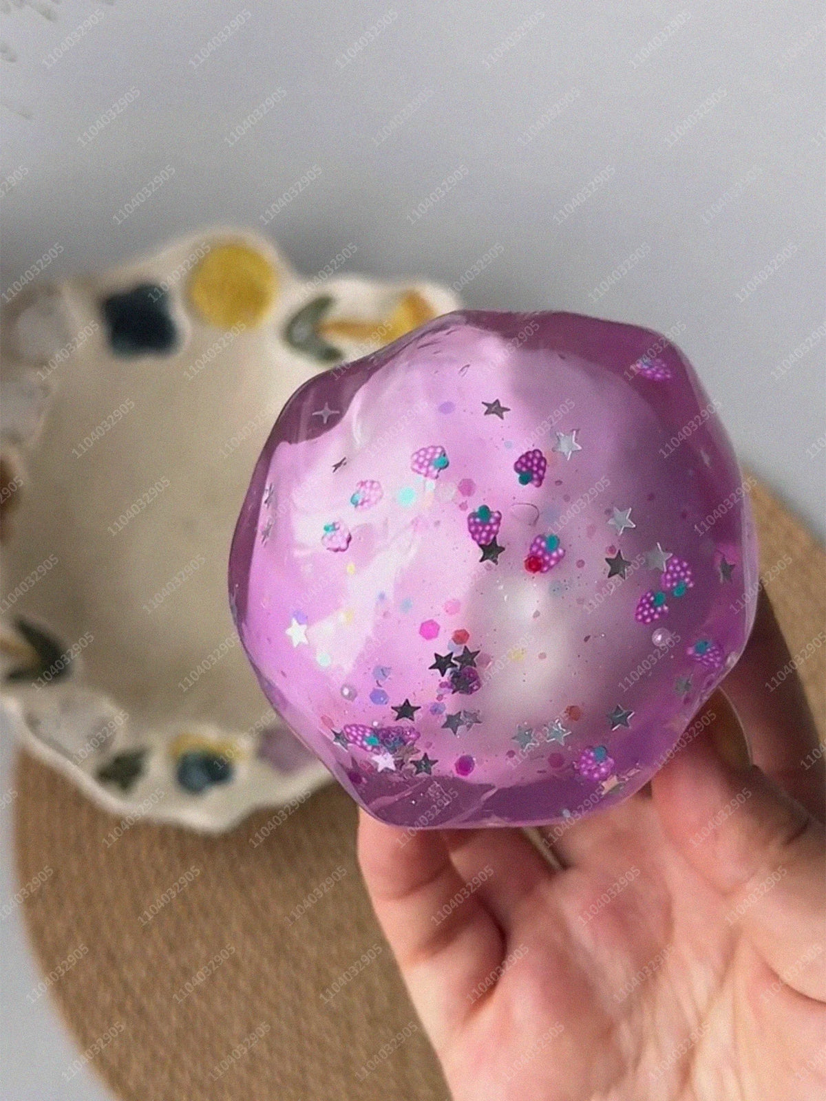 A translucent purple stress ball filled with glitter and small candies is held in a hand against a light background.