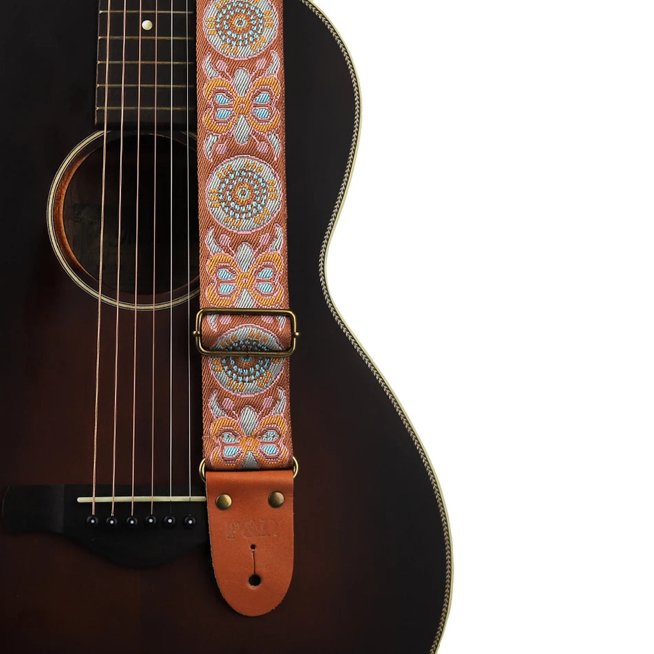 An embroidered guitar strap featuring intricate patterns in orange, blue, and white thread with leather ends.