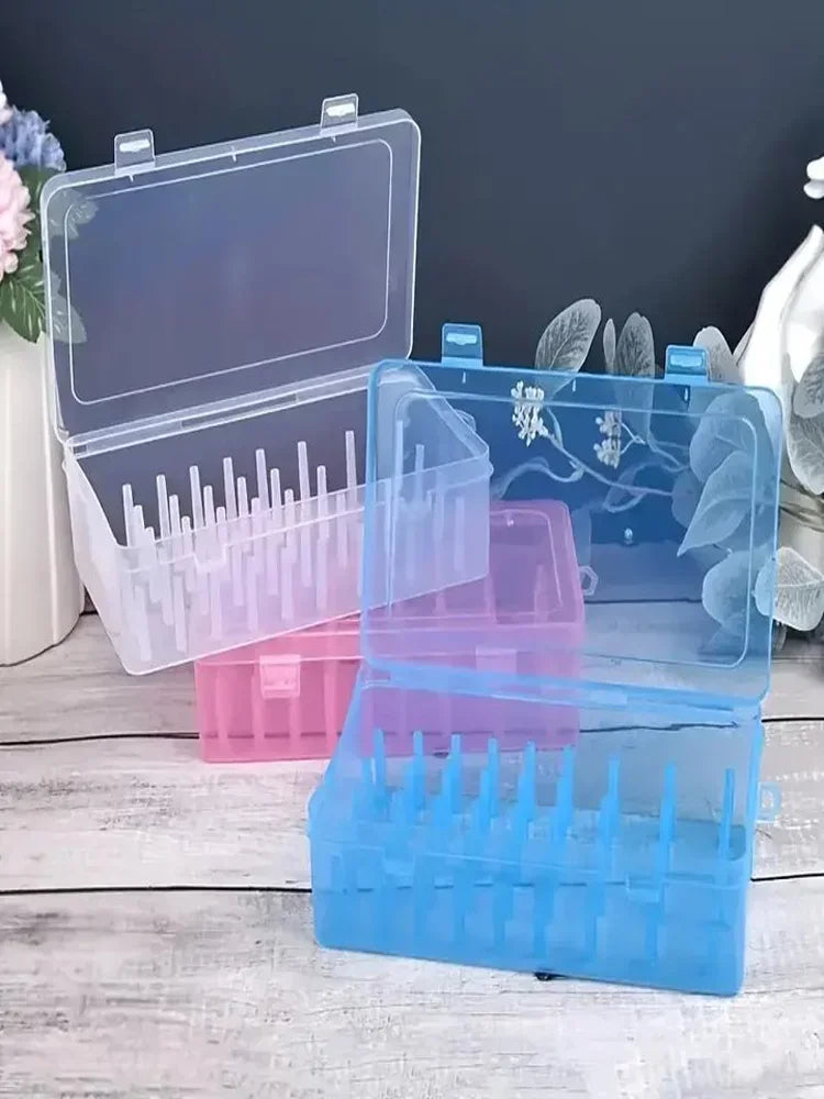 A set of transparent sewing thread organizers in pink and blue plastic with lids, showing various bobbins and compartments.