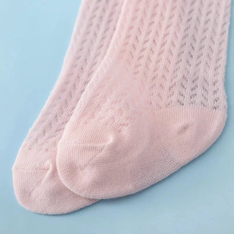 A close-up of a pair of light pink baby girl lace knee socks with a textured knit pattern.