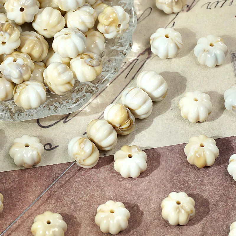 A collection of small, pale yellow and white gold-traced pumpkin resin beads for jewelry making displayed on a glass platter.