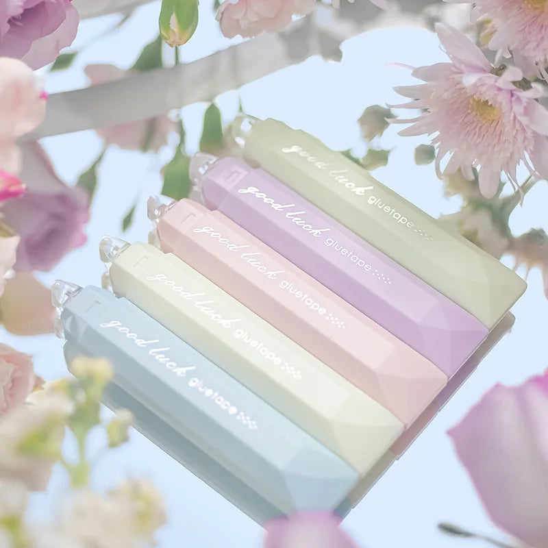 A pack of four pastel colored rotating double-sided adhesive dot tape glue rollers displayed against a soft floral background