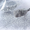 A close-up shot of holographic fine glitter powder being squeezed onto a surface for crafting projects.