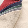 A stack of folded classic cotton-linen dinner napkins in various shades of red, blue, green, and gray.