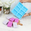 A blue silicone soap mold with six lace patterns is held by a hand, alongside several pink and white handmade soaps.