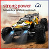 A yellow and black brushless 4WD monster truck RC car with LED headlights driving on a rough dirt road.