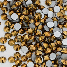 A close-up view of various flatback rhinestones in gold and silver tones for nail art and crafts.