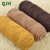 Three skeins of soft cotton blend yarn in shades of mustard yellow, beige, and dark brown on a light carpet.
