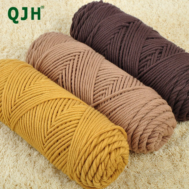 Three skeins of soft cotton blend yarn in shades of mustard yellow, beige, and dark brown on a light carpet.