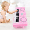 A baby is playing a pink 37-key electronic keyboard with a microphone on a white wooden surface.