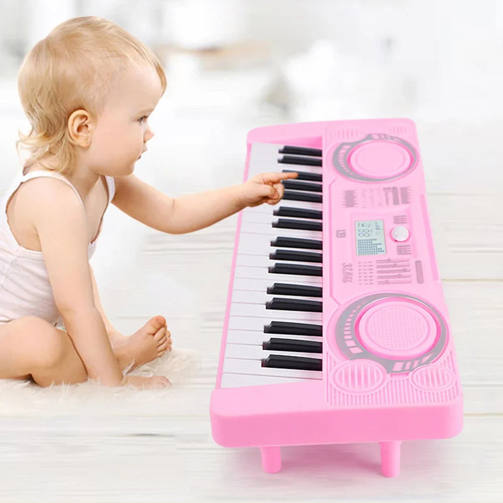 A baby is playing a pink 37-key electronic keyboard with a microphone on a white wooden surface.