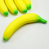 A yellow squishy banana stress reliever toy with green accents is shown against a white background.