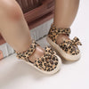 A pair of leopard print soft sole baby sneakers shown on a person's foot.