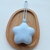 A light blue star-shaped portable pacifier and teether hanging on a wooden tray.