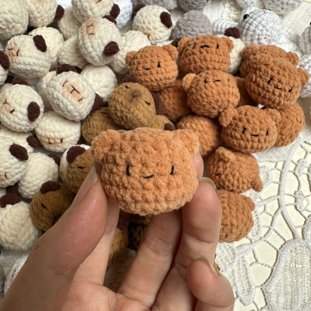 A hand holds a small, handcrafted crochet animal keychain made of brown yarn.