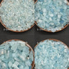 A collection of natural aquamarine chips in various sizes and shades, displayed in four separate bowls.