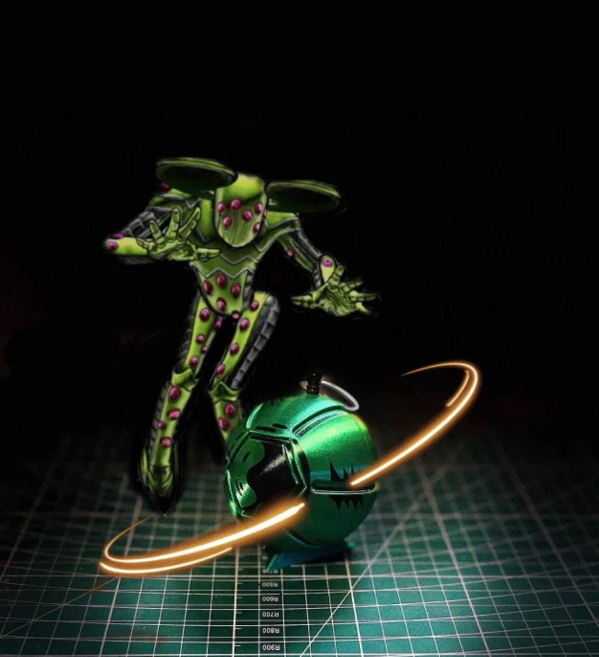 A green, insect-like figure is positioned above a glowing orange ring around a metallic sphere on a grid surface.