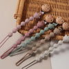 A set of silicone bear paw pacifier clips with wooden accents arranged on a woven tray.