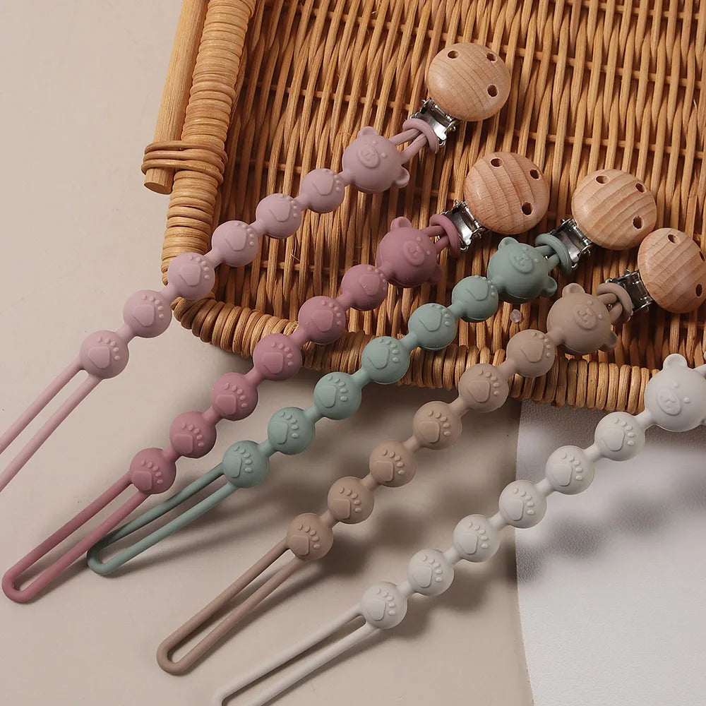 A set of silicone bear paw pacifier clips with wooden accents arranged on a woven tray.