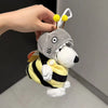 A gray and yellow striped plush toy with a dog face is being held by a hand, featuring a white cord and yellow pom-poms.