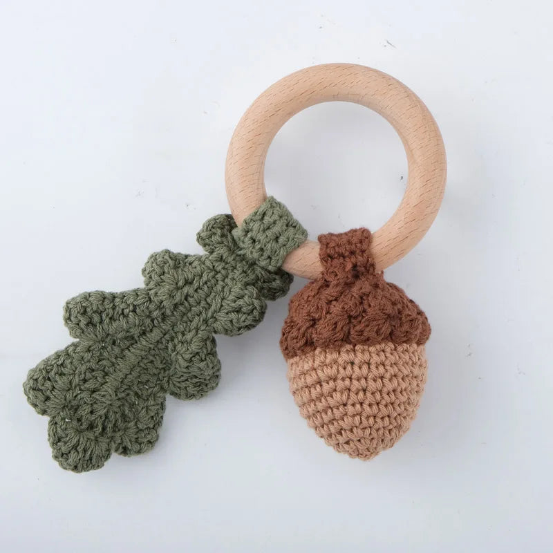 A wooden baby rattle and teether ring featuring a light wood loop and a textured green and brown knitted fruit design.