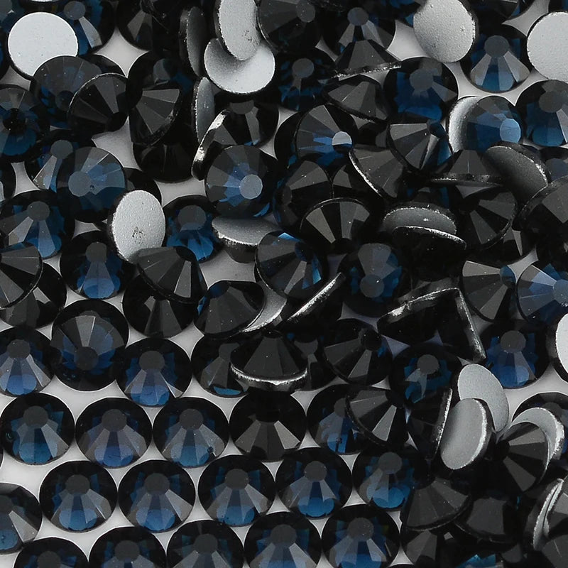 A close-up view of dark blue and black glass crystal flatback rhinestones scattered on a white surface.
